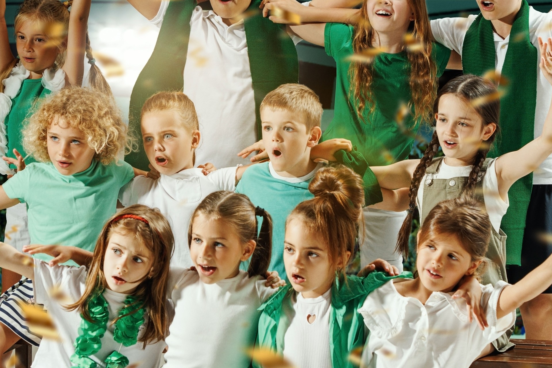 Children dressed in green and white cheering enthusiastically and hugs and golden confetti falling around them.