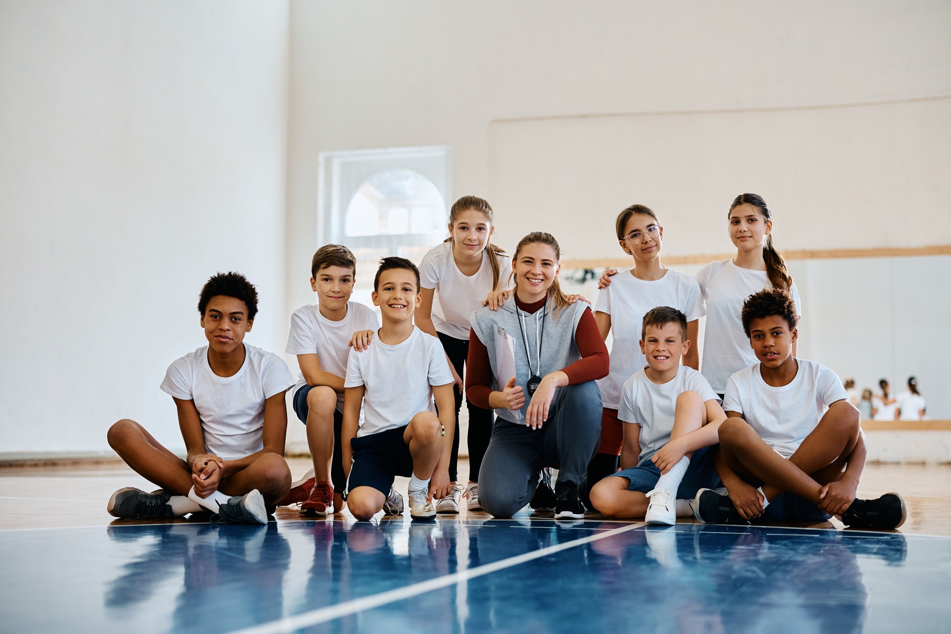 Portrait of happy sports teacher with group of kids at school gym looking at camera.